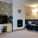 Photo of Easterfield Road front living room featuring a modern built in fireplace, a sofa, a TV Unit and TV. The walls are papered with a tasteful floral pattern and plain around the chimney breast