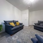 Bankhead Road living room. There is laminate flooring, a large floor rug and a small leather sofa and two matching armchairs. The walls have been newly painted in white