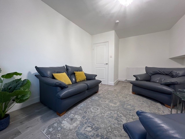 Bankhead Road living room. There is laminate flooring, a large floor rug and a small leather sofa and two matching armchairs. The walls have been newly painted in white